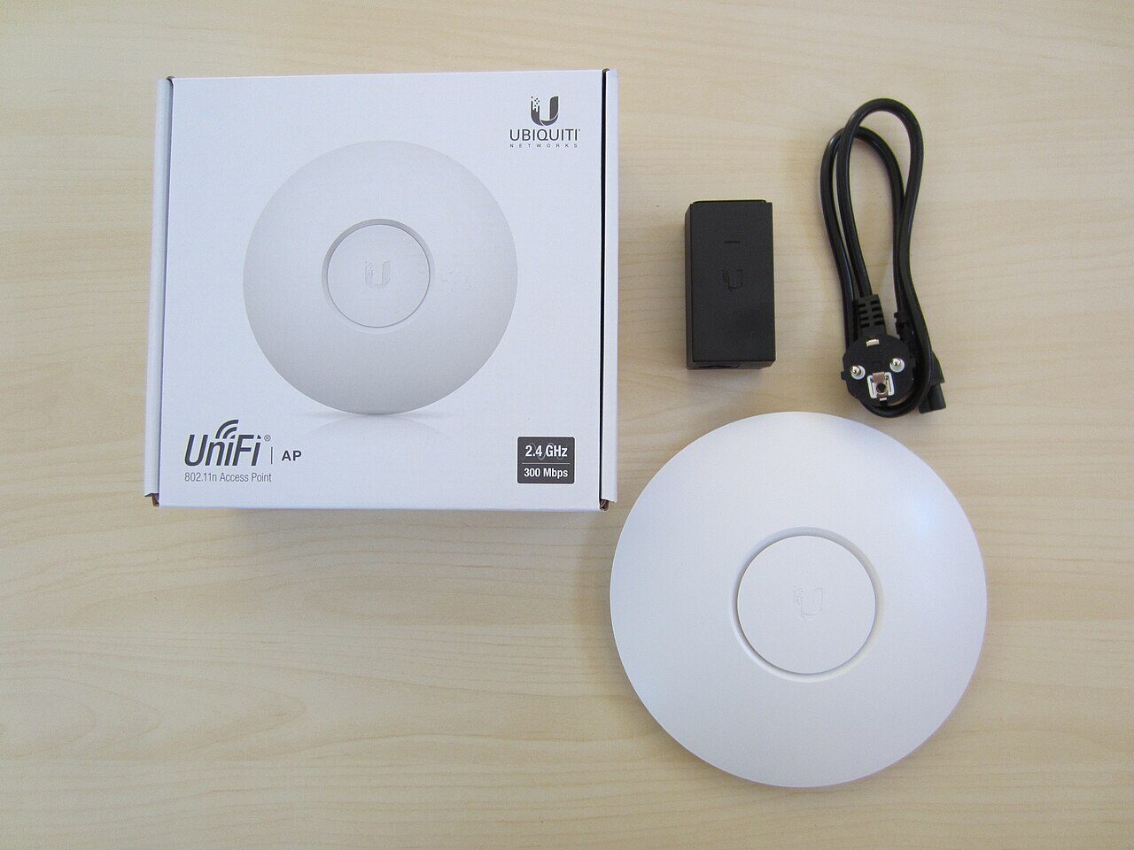 Un AP UniFi rotund și alb, de primă generație, lângă cutia lui, adaptorul PoE și cablul de alimentare